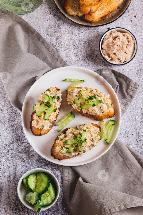 Скачать Салат из печени трески, яиц и огурцов с тостами на тарелке, установленной на столешнице, в вертикальном положении фотосток Ozero