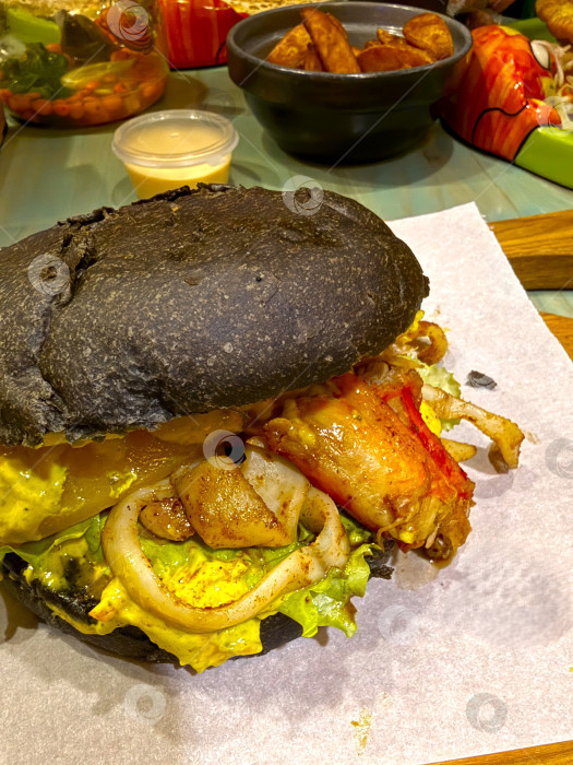 Скачать Изысканный бургер из морепродуктов с булочкой в чернилах черного кальмара фотосток Ozero