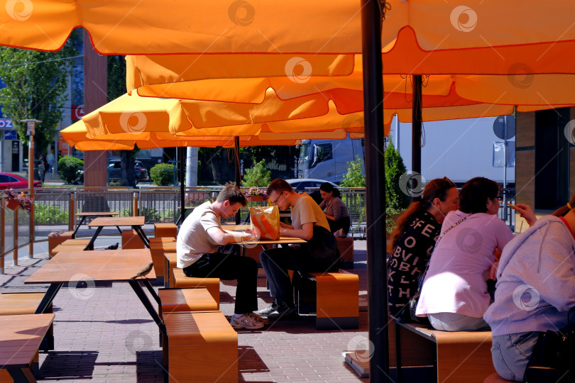 Скачать Солнечный летний день под зонтиками в кафе, общение, быстрые закуски и приятная атмосфера. фотосток Ozero