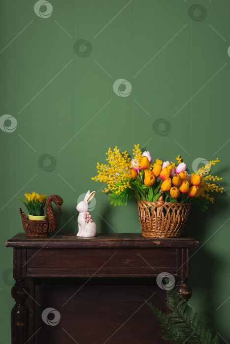 Скачать Декоративные элементы антикварного деревянного стола в эко-стиле с тюльпанами, мимозой и пасхальным фарфоровым кроликом на зеленой стене фотосток Ozero