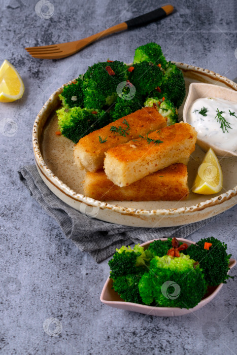 Скачать Хрустящие рыбные палочки в панировке подаются с брокколи, приготовленной на пару, йогуртовым соусом и долькой лимона фотосток Ozero