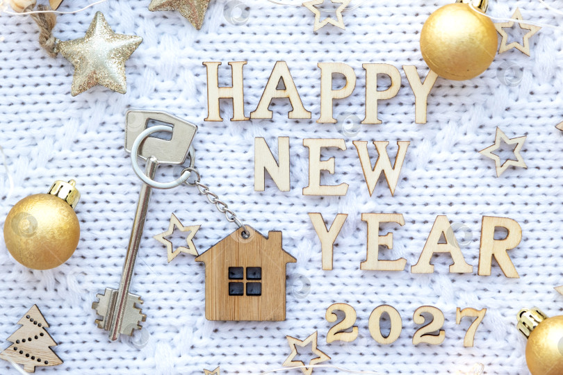 Скачать Ключ от дома с брелком, коттедж на праздничном фоне со звездами, огоньками гирлянд. Деревянные буквы на Новый 2027 год, поздравительная открытка. Покупка, строительство, переезд, ипотека, страхование фотосток Ozero