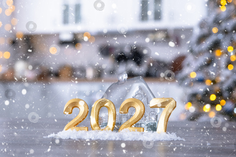 Скачать Золотая цифра 2027 и крошечный домик на фоне уютной белой кухни с рождественской елкой и рождественским декором из гирлянд. Жилье, интерьер, ремонт, ипотека, аренда в Новом году фотосток Ozero