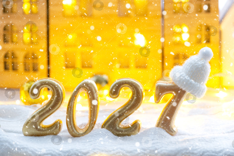 Скачать Золотые фигурки с цифрами Нового 2027 года на фоне крошечного домика с теплым светом и гирляндами. Поздравительная открытка, С Новым годом, уютный дом фотосток Ozero