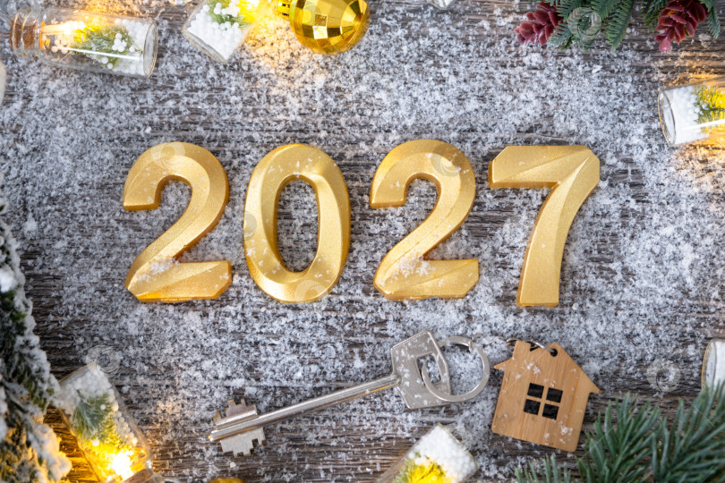 Скачать Золотые цифры на Новый 2027 год и ключ от дома с миниатюрной формой дома на праздничном сером деревянном фоне, флэтлей, гирлянды, поздравительная открытка. Жилье, недвижимость, переезд, ипотека, страхование. фотосток Ozero