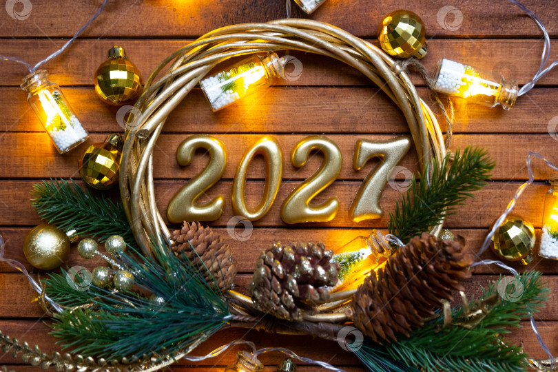 Скачать Деревянные цифры с Новым годом 2027 на уютном, праздничном коричневом деревянном фоне в венке из пайеток, снега, огней гирлянд. Поздравление, открытка. Календарь, обложка фотосток Ozero