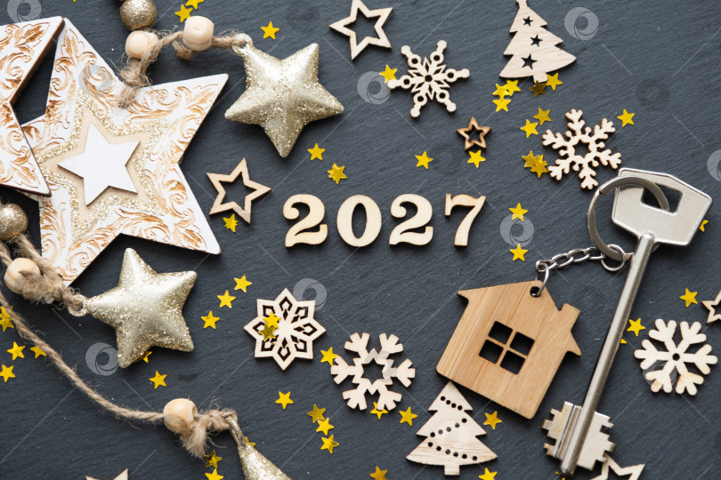 Скачать Ключ от дома с брелком-дача на праздничном черном фоне со звездами, огоньками гирлянд. Деревянные буквы на Новый 2027 год, поздравительная открытка. Покупка, строительство, переезд, ипотека, страхование фотосток Ozero
