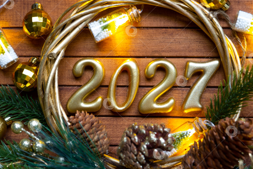 Скачать Деревянные цифры с Новым годом 2027 на уютном, праздничном коричневом деревянном фоне в венке из пайеток, снега, огней гирлянд. Поздравление, открытка. Календарь, обложка фотосток Ozero