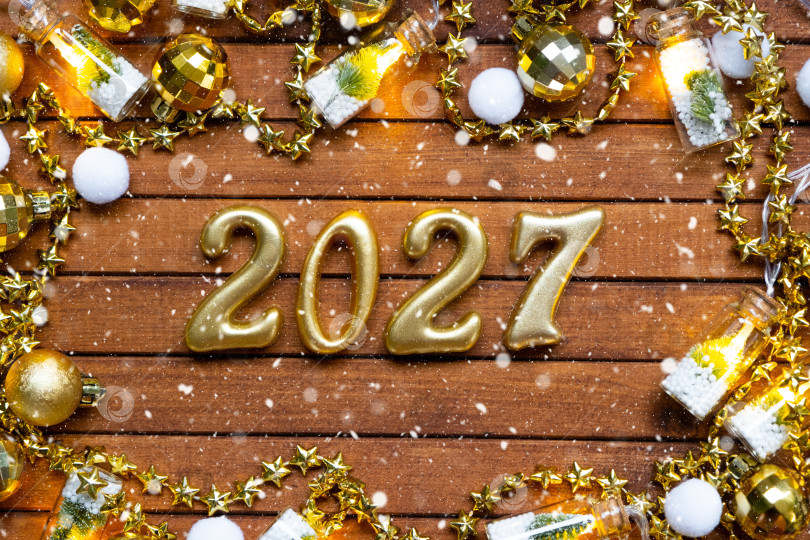 Скачать Деревянные цифры с Новым 2027 годом на уютном, праздничном коричневом деревянном фоне с блестками, снегом, огнями гирлянд. Поздравление, открытка. Календарь, обложка фотосток Ozero