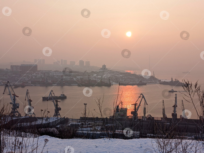 Скачать Вид на бухту, порт и мыс с силуэтами небоскребов на фоне зимнего рассветного неба во Владивостоке фотосток Ozero