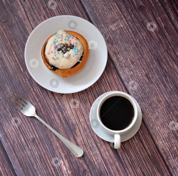 Скачать Булочка с корицей и сливочным сыром на тарелке, рядом с вилкой и чашкой черного кофе. фотосток Ozero