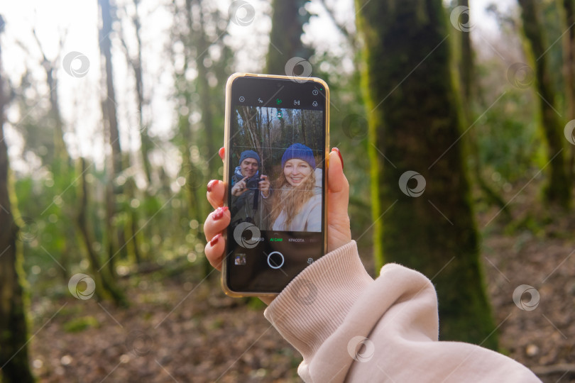 Скачать Женщина фотографирует своих друзей в лесу с помощью смартфона. фотосток Ozero