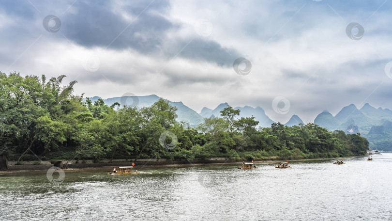Скачать По живописной реке плывут бамбуковые плоты и туристические суда. фотосток Ozero