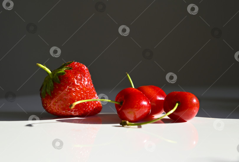 Скачать Красная черешня и ягода клубники на белом фоне в лучах солнца фотосток Ozero
