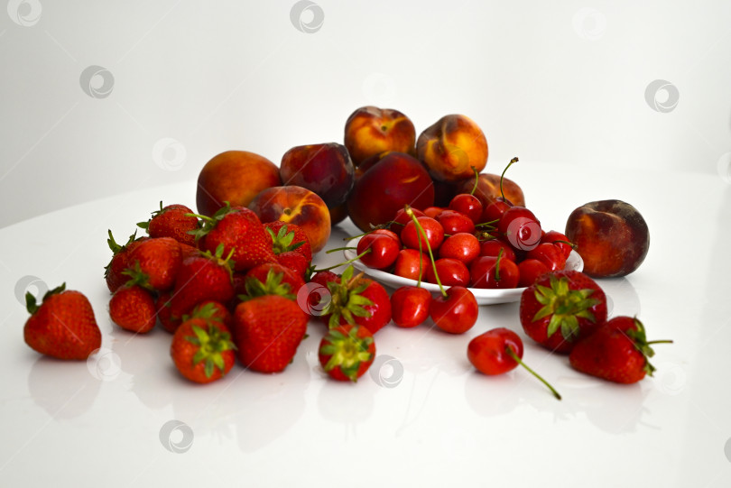 Скачать Набор свежих сезонных ягод и фруктов на белом столе фотосток Ozero