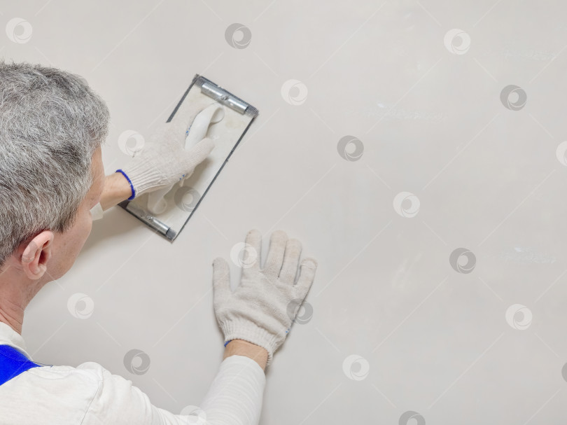 Скачать Крупным планом видны руки рабочего и инструмент для шлифовки шпаклевки. фотосток Ozero