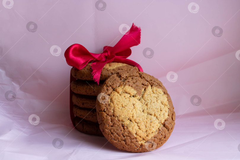 Скачать Круглое овсяное печенье с сердечком, перевязанное красной лентой-бантиком, на розовом фоне из мятой бумаги. Праздничная идея для Дня Святого Валентина, 8 марта и Рождества фотосток Ozero