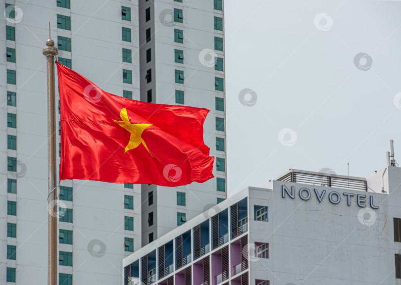 Скачать Вьетнам, 04 сентября 2025 года.Вьетнамский флаг с красным фоном и жёлтой звездой. Видны здания отелей в Нячанге фотосток Ozero
