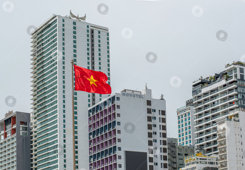 Скачать Вьетнам, 04 сентября 2025 года.Вьетнамский флаг с красным фоном и жёлтой звездой. Видны здания отелей в Нячанге фотосток Ozero