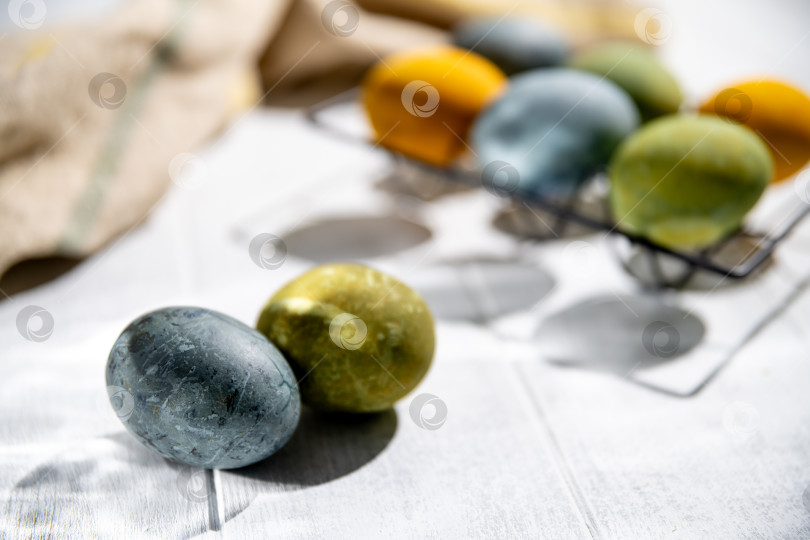 Скачать Пасхальные яйца, окрашенные натуральным способом, сохнут на белом деревянном столе, создавая праздничную атмосферу для празднования Пасхи, на фоне бежевой скатерти. фотосток Ozero