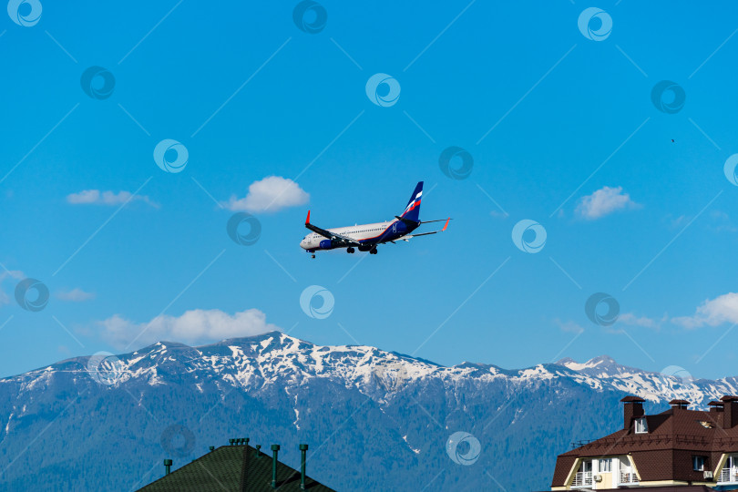 Скачать Boeing 737-8LJ(WL) пролетает над жилыми домами на фоне заснеженных вершин Кавказских гор.Аэрофлот - Российские авиалинии. Шасси и закрылки самолета выпущены. Сочи, Россия - 18 мая 2021 г. фотосток Ozero