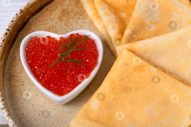 Скачать Традиционные русские тонкие блинчики (крепы) и красная икра в форме сердца крупным планом на керамической тарелке фотосток Ozero