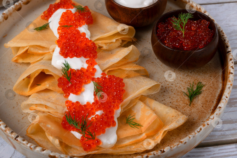 Скачать Традиционные русские тонкие блинчики (крепы) со сметаной и красной икрой на керамической тарелке фотосток Ozero