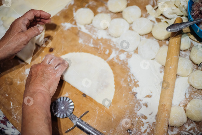 Скачать Крупный план женских рук пожилой женщины, раскатывающей тесто деревянной скалкой. Приготовление домашних пирогов и чебуреков. фотосток Ozero