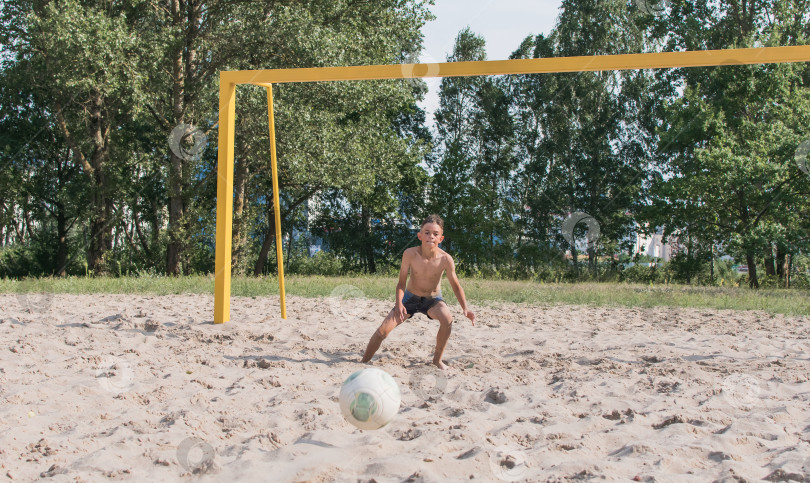 Скачать Маленький мальчик играет в футбол на песке фотосток Ozero
