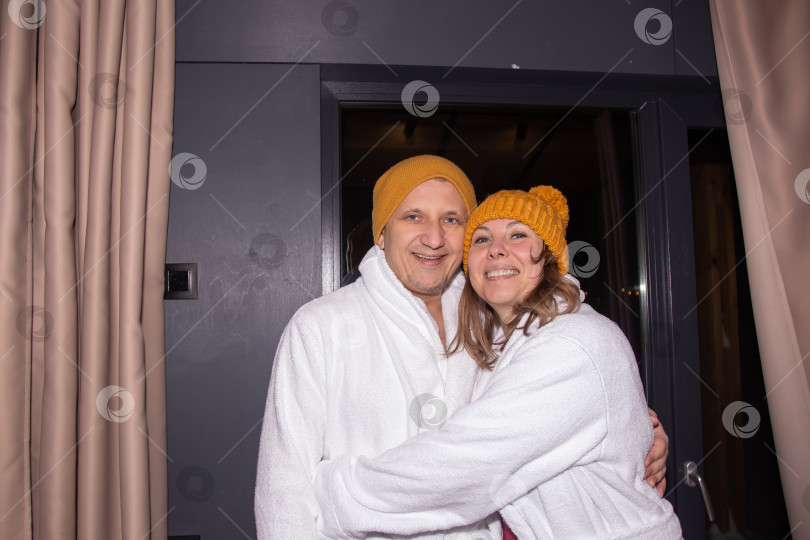 Скачать Пара отдыхает на террасе загородного дома зимним вечером. Красивая женщина и красивый мужчина расслабленно стоят на террасе деревянного коттеджа. Зимний курорт. фотосток Ozero