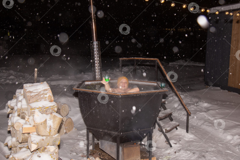Скачать Ванна. Мужчина плавает в гидромассажной ванне, расслабляясь. Мужчина принимает горячую ванну в заснеженном лесу на открытом воздухе. Зимние каникулы в заснеженных горах. фотосток Ozero