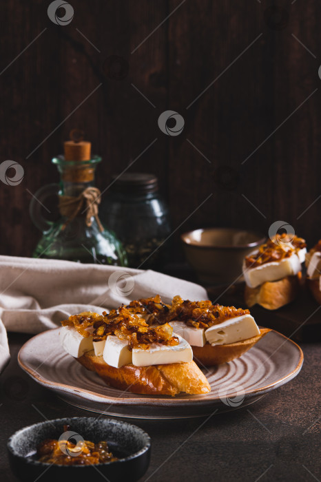 Скачать Закусочные бутерброды с сыром бри и карамелизированным луком на тарелке на столе, вид сверху фотосток Ozero