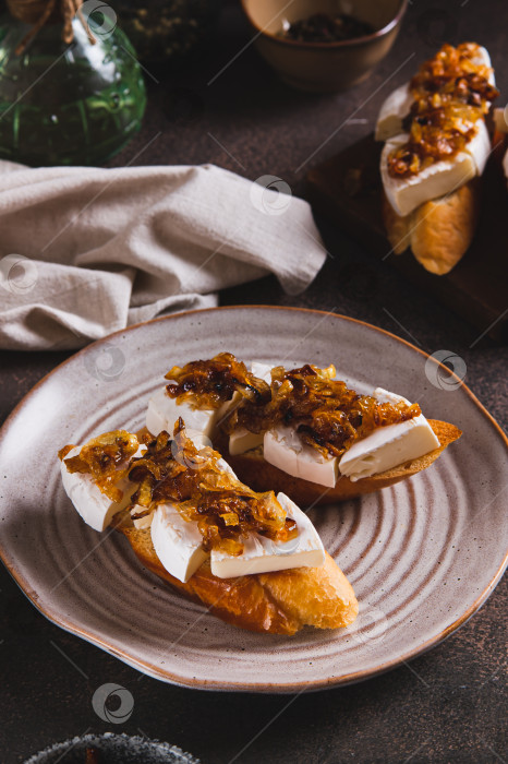 Скачать Тосты со сливочным сыром бри и карамелизированным луком на тарелке на столе, вид сверху фотосток Ozero