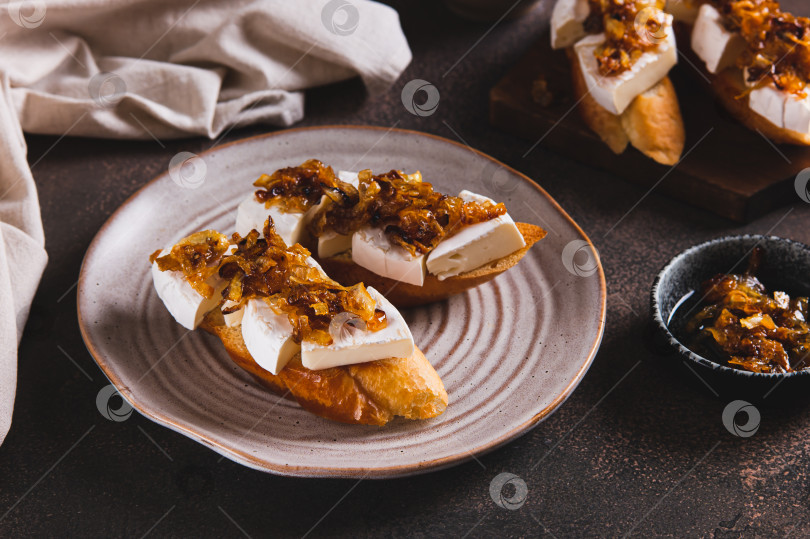 Скачать Тосты со сливочным сыром бри и карамелизированным луком на тарелке на столе фотосток Ozero