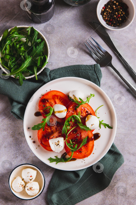Скачать Салат капрезе с помидорами, моцареллой и рукколой на тарелке, установленной на столе в вертикальном положении фотосток Ozero
