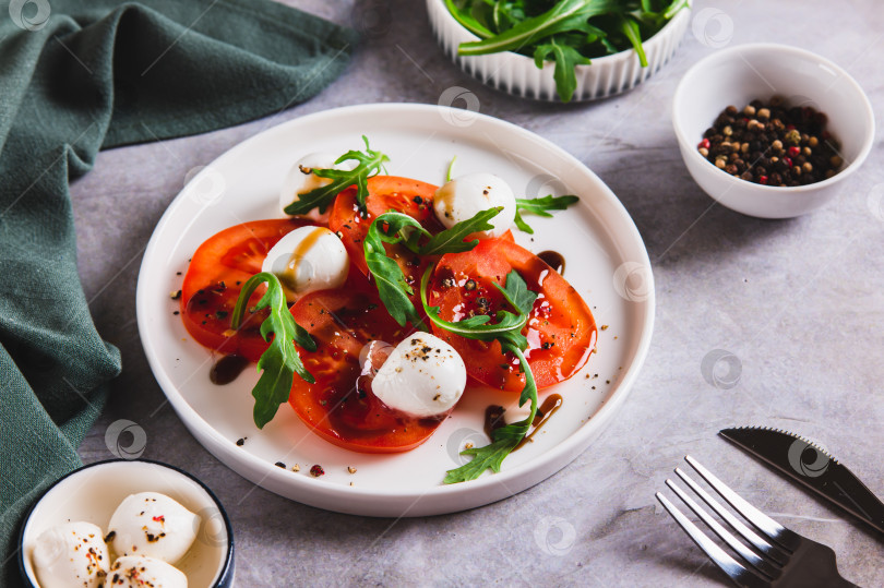 Скачать Салат капрезе с помидорами, моцареллой и рукколой на тарелке на столе фотосток Ozero