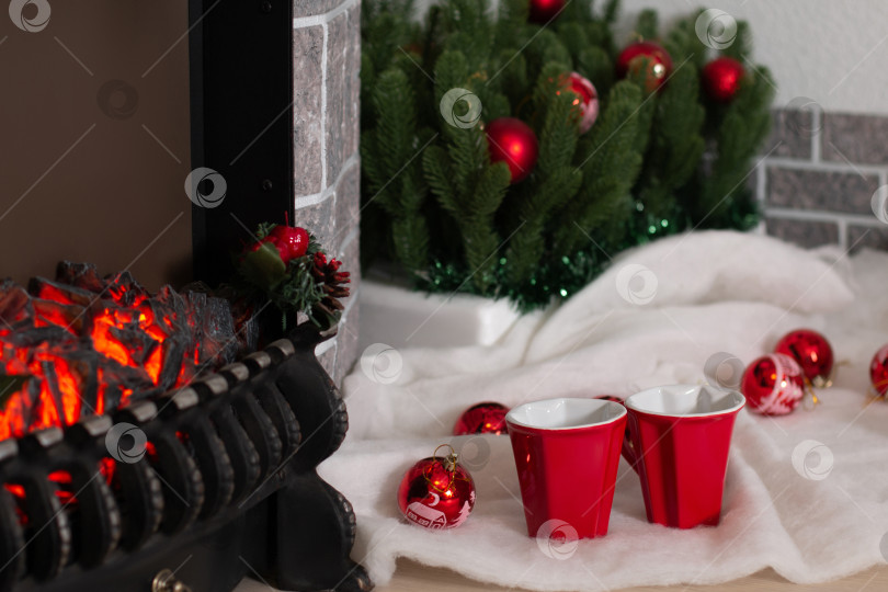 Скачать Две красные чашки для влюбленных у горящего камина и рождественские украшения фотосток Ozero