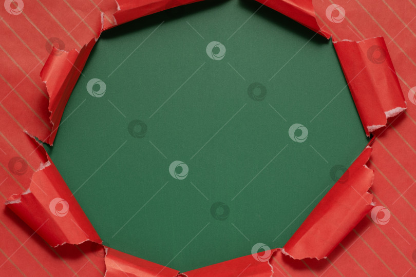 Скачать Порванная красная оберточная бумага, открывающая зеленый фон во время приготовления праздничного подарка фотосток Ozero