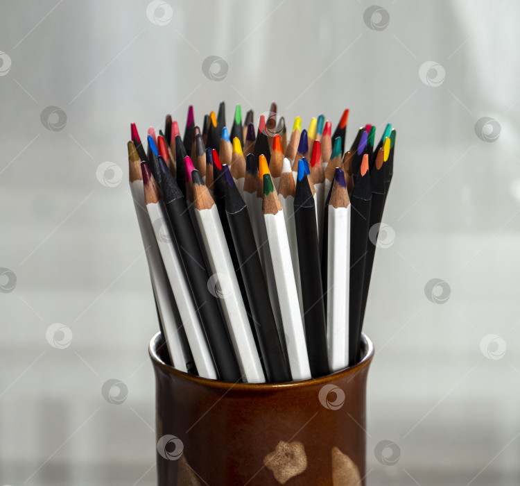 Скачать Цветные деревянные карандаши плотно уложены в круглую глиняную подставку. Корпуса карандашей раскрашены в черный и белый цвета. Фон для творчества. фотосток Ozero