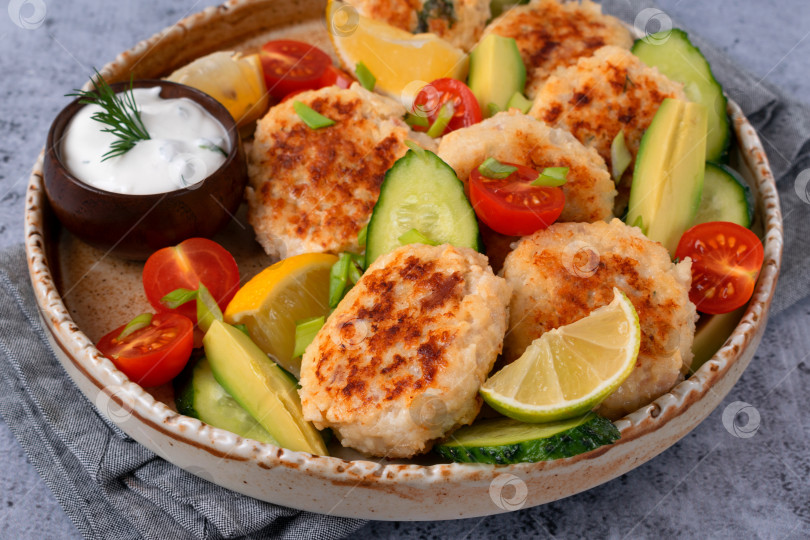 Скачать Жареные рыбные котлеты, приготовленные с беконом, сыром и зеленью, подаются со свежими овощами, дольками лимона и сметанным соусом фотосток Ozero