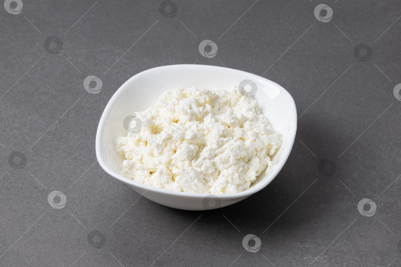 Скачать Творог в белой миске на серой поверхности в кухонной обстановке, демонстрирующий свежие молочные продукты, готовые к подаче фотосток Ozero