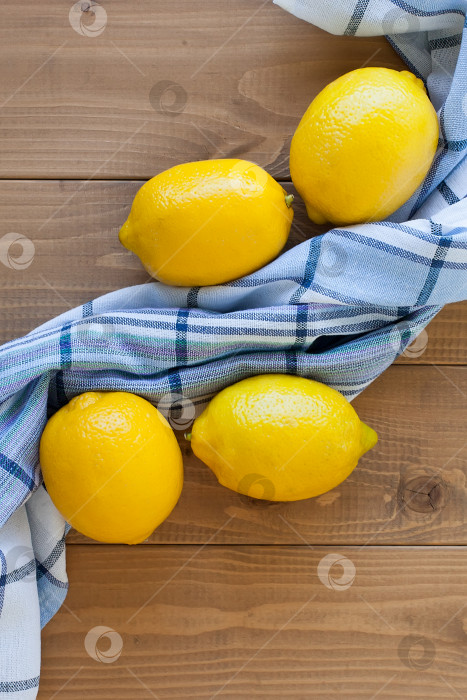Скачать Группа из четырех целых желтых лимонов на деревянном фоне рядом с полотенцем в клетку фотосток Ozero