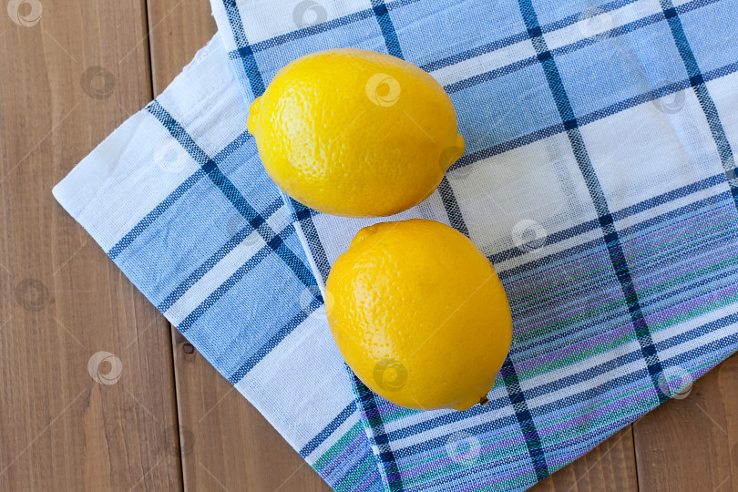 Скачать Два цитрусовых лимона на деревянном столе на кухонном полотенце. фотосток Ozero