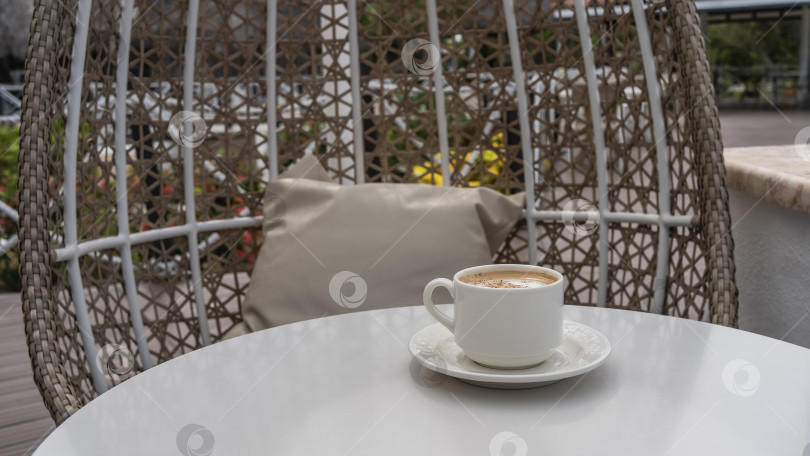 Скачать Кофейная чашка с капучино на блюдце на белом круглом столике. фотосток Ozero