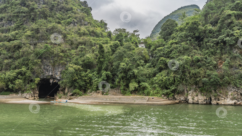 Скачать Пещера в скале на берегу реки. Лодки у темного входа фотосток Ozero