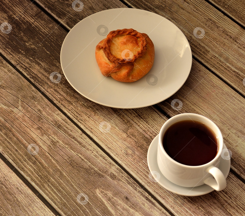 Скачать Мясной пирог Элеш на тарелке и чашка черного чая на блюдце на деревянном столе. фотосток Ozero