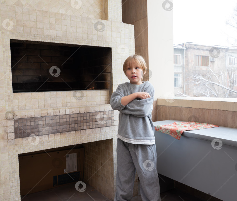 Скачать Маленький мальчик стоит на балконе рядом с камином. Ребенку холодно зимой фотосток Ozero