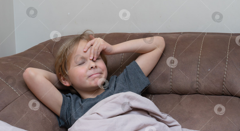 Скачать Маленький мальчик с головной болью лежит на диване, касаясь лба. Больной ребенок плохо себя чувствует дома фотосток Ozero