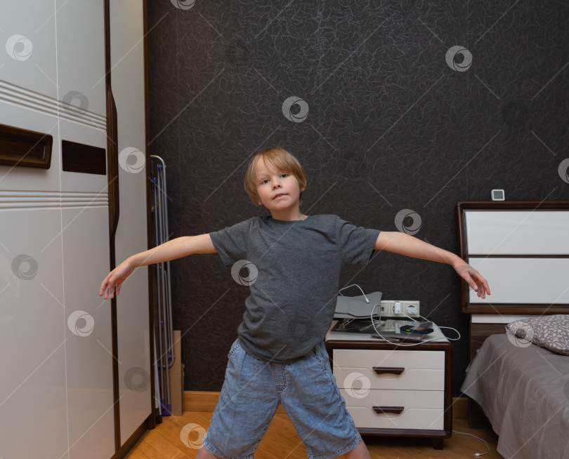 Скачать Маленький мальчик стоит в спальне с широко раскинутыми руками. Ребенок притворяется, что летит или балансирует фотосток Ozero