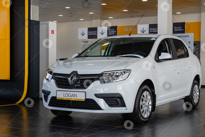 Скачать Белый Renault Logan в автосалоне Renault. На заднем плане - рабочие места сотрудников автосалона. Автомобиль крупным планом. Автосалон Renault в Мега Адыгея. фотосток Ozero